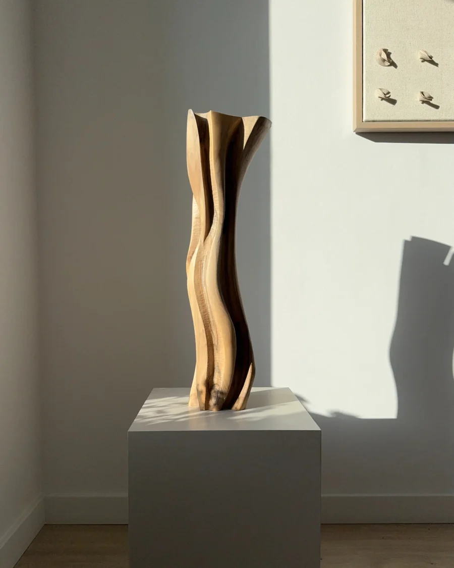 Walnut wood vase with dried grasses, tall hand-carved form casting organic shadow on wall