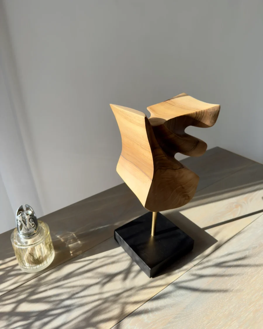 Walnut sculpture Velora with natural light casting dynamic shadows on surface and wall