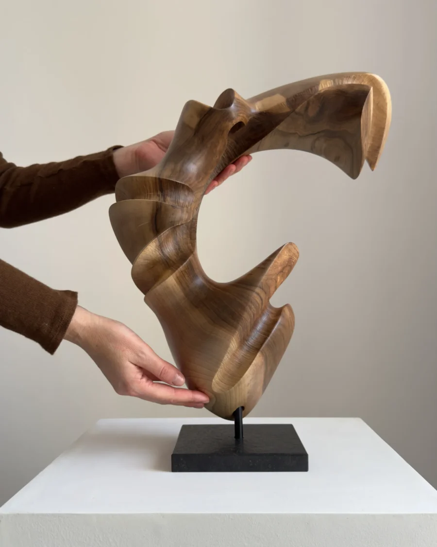 Hand holding abstract wood sculpture in walnut, showing scale and organic carved form