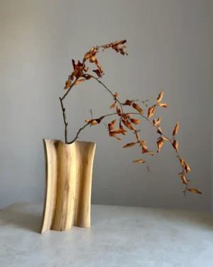 Hand-carved walnut wood vase with dried branch, minimalist sculptural form, natural grain detail