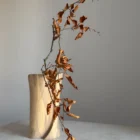 Back view of hand-carved walnut vase with dried branch, organic shape and flowing wood grain