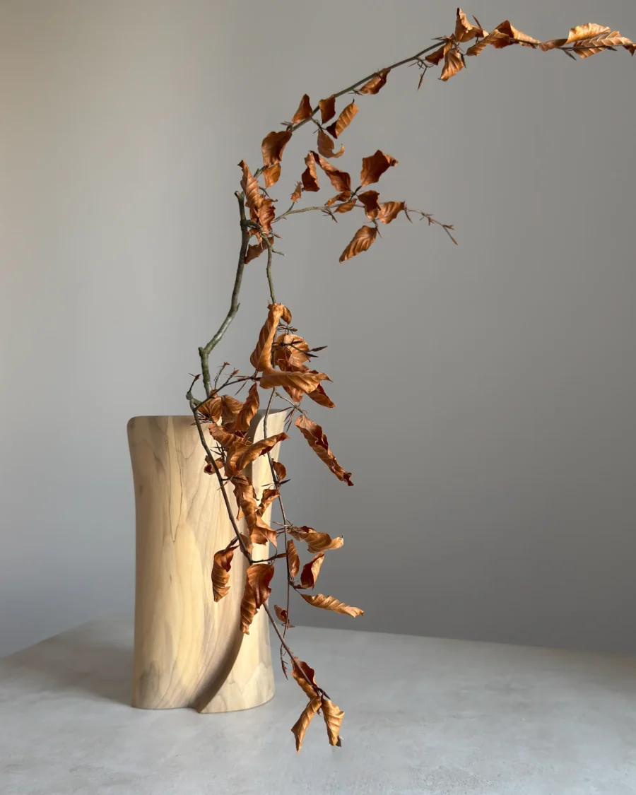 Back view of hand-carved walnut vase with dried branch, organic shape and flowing wood grain