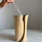 Hand placing glass tube inside carved walnut vase, functional wooden sculpture for fresh flowers