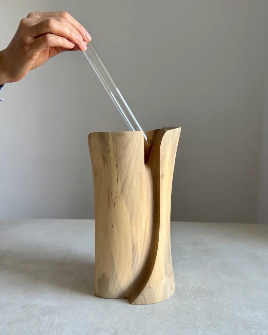 Hand placing glass tube inside carved walnut vase, functional wooden sculpture for fresh flowers