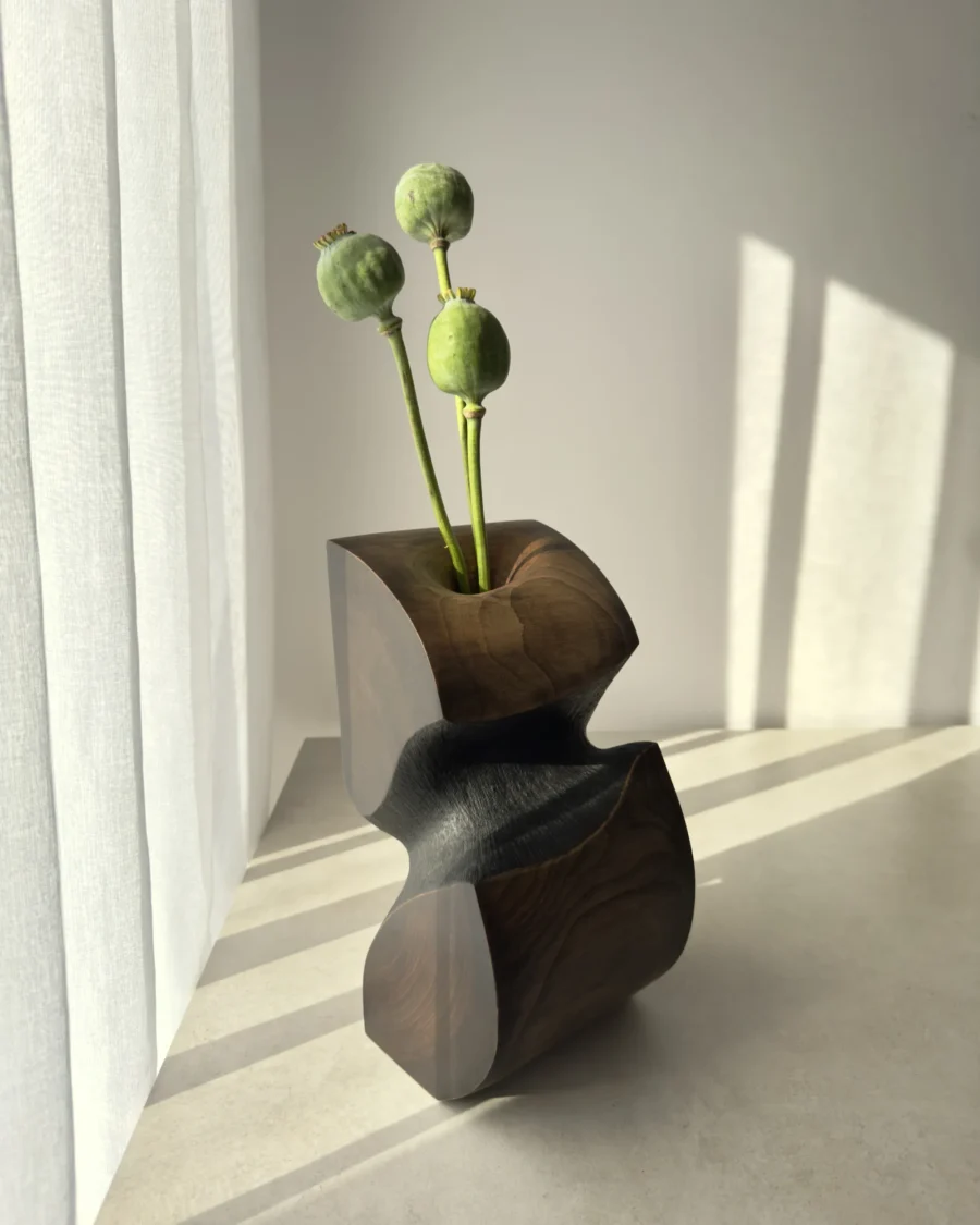 Ember Hollow hand-carved apple wood sculptural vase with poppy seed pods, shown in warm natural light with black waxed and natural wood surfaces.
