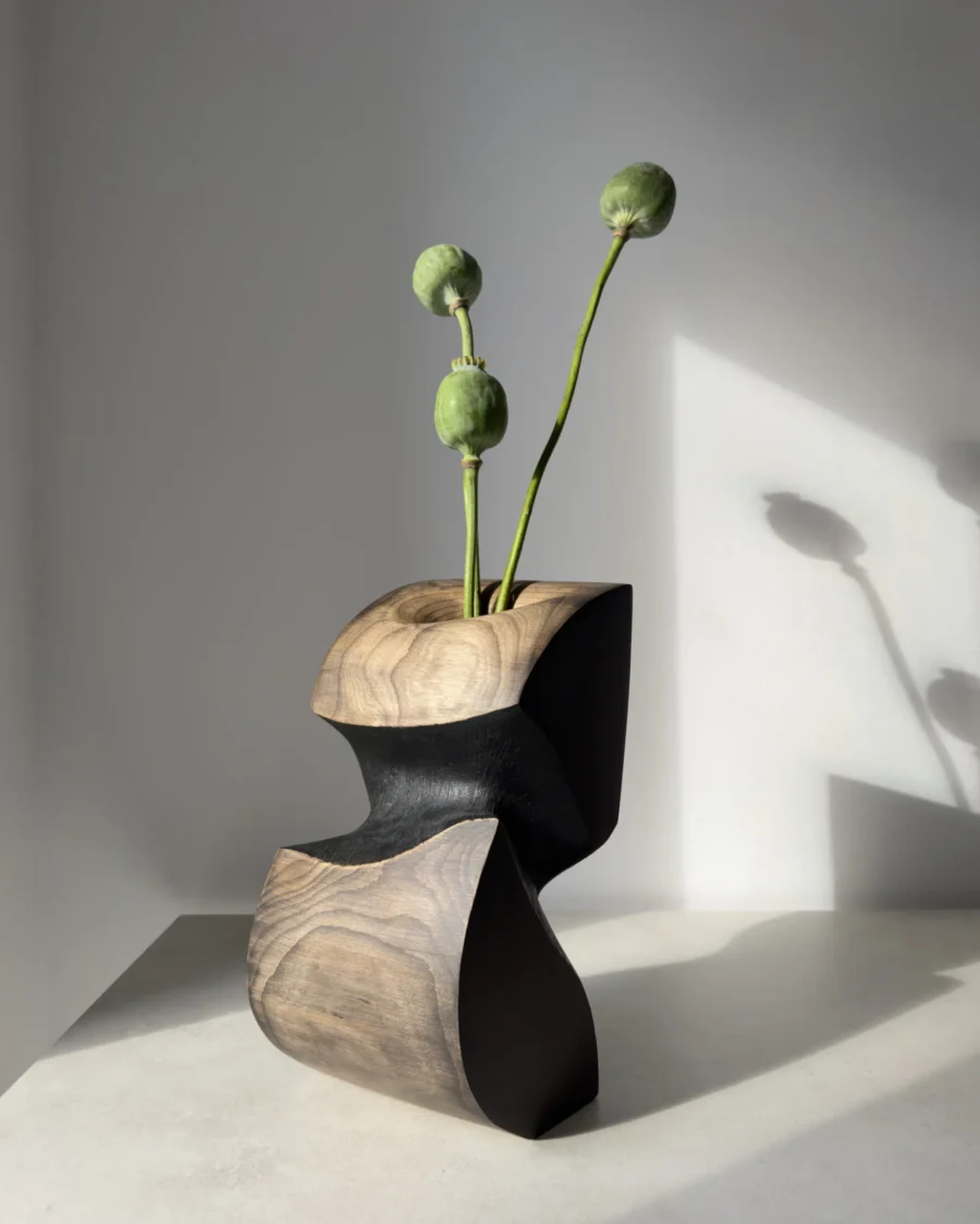 Side view of Ember Hollow sculptural apple wood vase with poppy seed pods, showing contrasting black waxed surfaces and visible natural wood grain.
