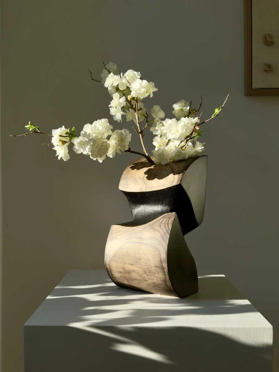 Artistic wooden vase styled with fresh flowers on neutral pedestal