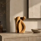 Hand-carved walnut wood sculpture Quiet Endurance displayed on a stone console in a contemporary Japandi interior with warm natural light.