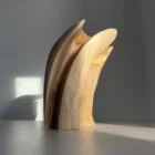 Side view of a hand-carved abstract wood sculpture in walnut, showing a soft curved shape and natural wood grain
