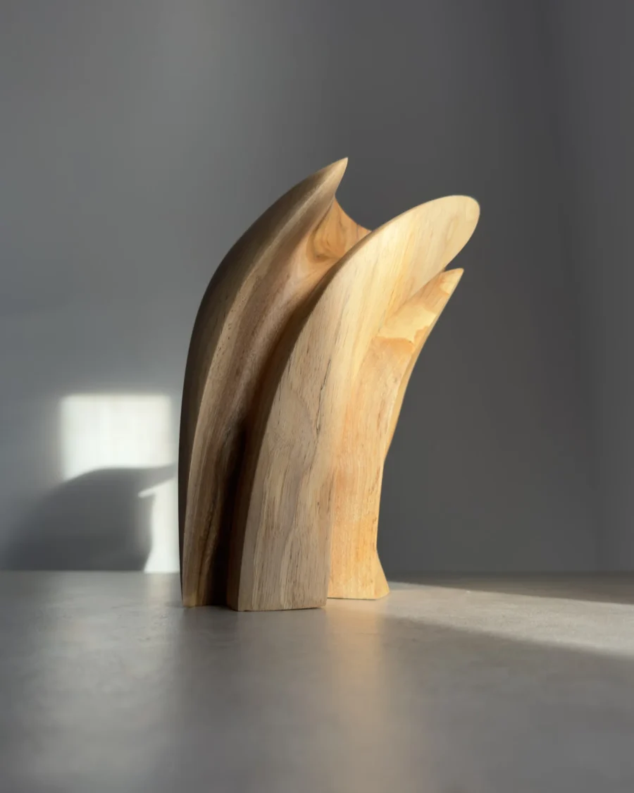 Side view of a hand-carved abstract wood sculpture in walnut, showing a soft curved shape and natural wood grain