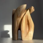 A hand-carved walnut wood sculpture “Quiet Endurance” in natural sunlight, showing its curved abstract form and flowing grain.