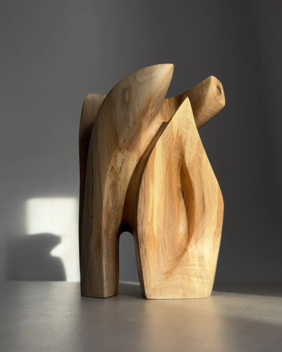 A hand-carved walnut wood sculpture “Quiet Endurance” in natural sunlight, showing its curved abstract form and flowing grain.