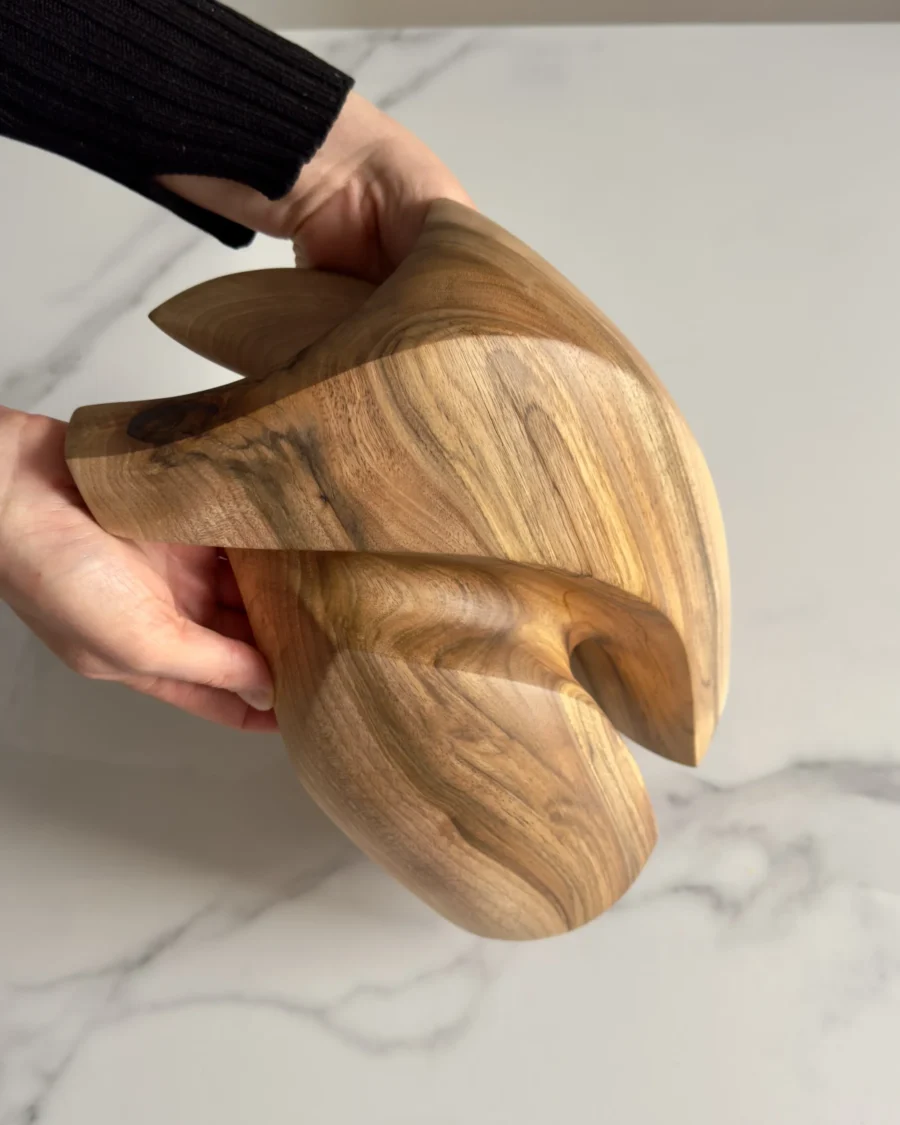 Close-up of a hand holding an abstract walnut sculpture, showing smooth surface and natural grain