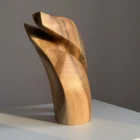 Walnut wood sculpture with visible grain contrast and organic curves, photographed in natural directional light.