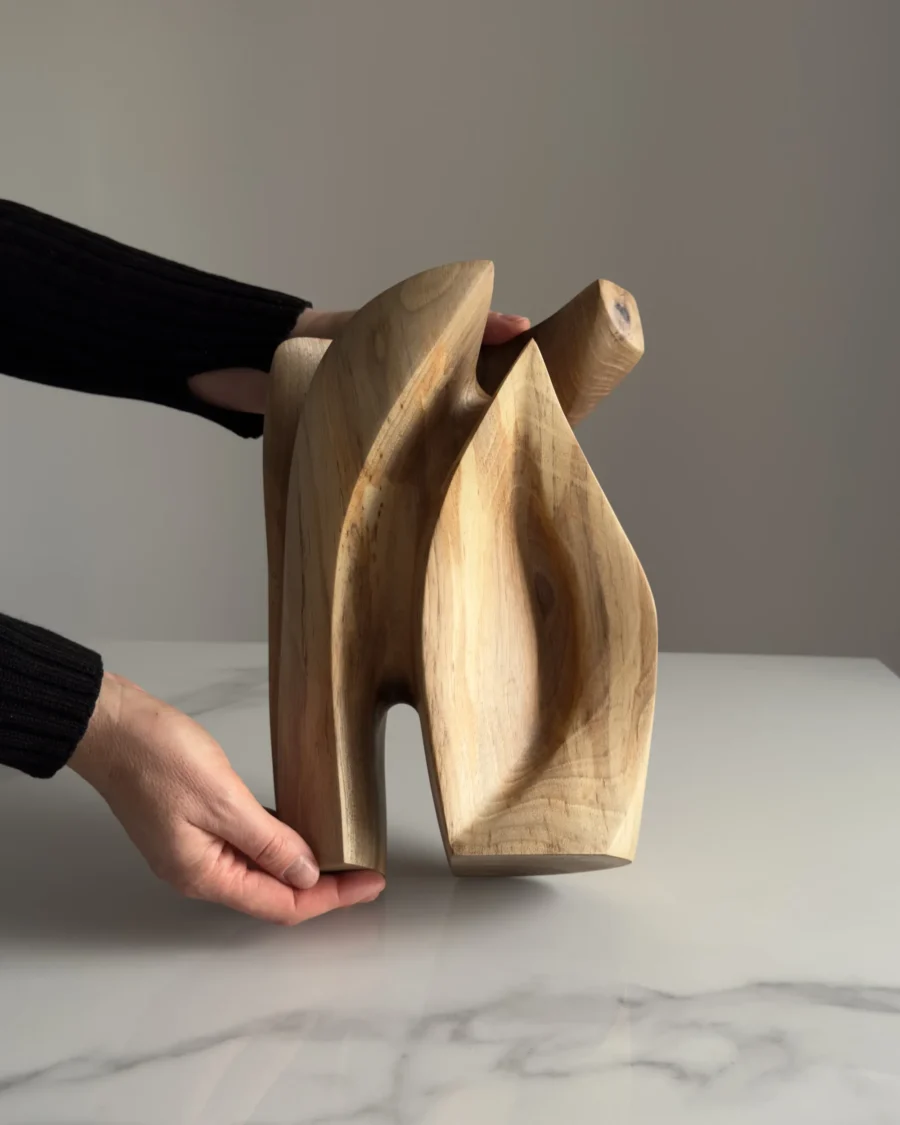 Hand holding a walnut wood sculpture to show scale and detail of the carved abstract form