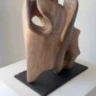 rebirth-wood-sculpture-back- iew-ewebohome Side view of a walnut sculpture on a raw stone base, highlighting contrast between wood and slate, white pedestal