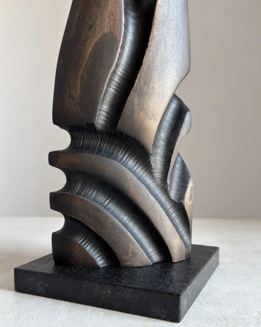 Close-up of Sentinel abstract beech wood sculpture showing polished granite base, repeating black carved recesses and contrasting warm wood tones