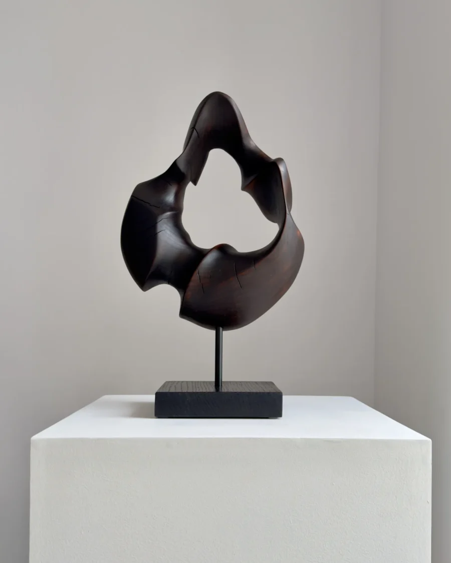 flame-memory-walnut-wood-sculpture-front-view-ewebohome Hand-carved walnut wood sculpture “Flame Memory” with fire-charred black surface on steel stand, front view in natural light