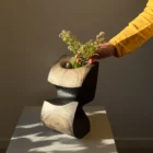 Hand placing flowers into sculptural apple wood vase showing scale and texture
