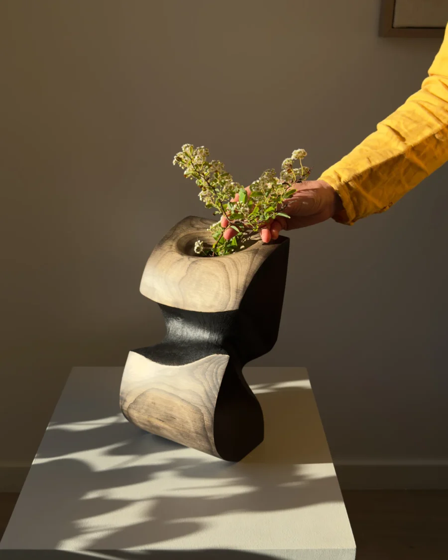 Hand placing flowers into sculptural apple wood vase showing scale and texture