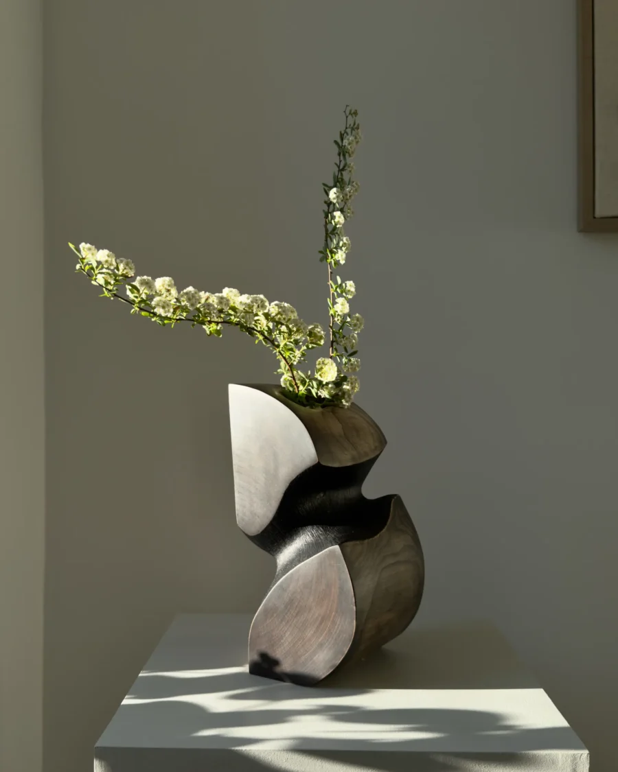 Hand carved apple wood sculptural vase with white flowers and dark textured interior in natural sunlight
