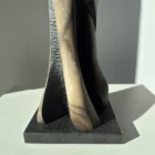 Detail of the lower section of “Noctivis” sculpture showing black textured carving, natural wood grain, and polished granite base.