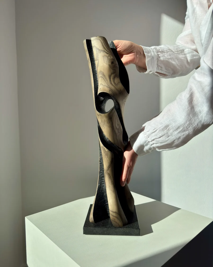 Artist holding “Noctivis” hand-carved wooden sculpture to show scale, texture, and natural light reflections.