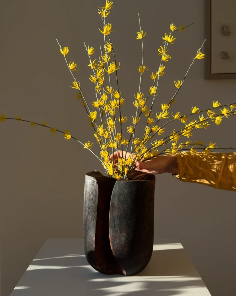 Hand carved walnut vessel with decorative yellow branches in calm interior setting
