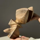 Hand-carved walnut wood sculpture Aureon held in both hands, showing scale, smooth organic forms and natural walnut grain in warm sunlight.