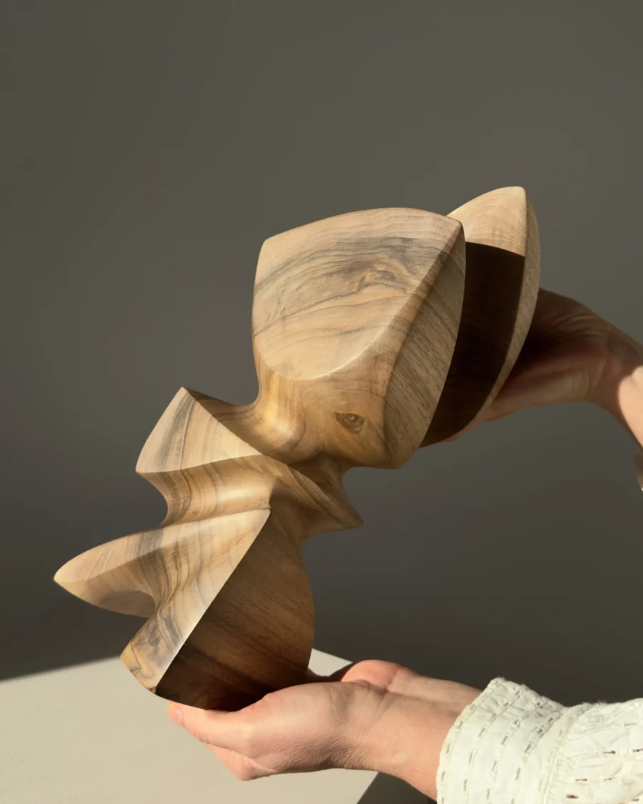 Hand-carved walnut wood sculpture Aureon held in both hands, showing scale, smooth organic forms and natural walnut grain in warm sunlight.