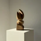 Hand-carved walnut wood sculpture Aureon shown from the front in warm natural light, with smooth organic curves and deep shadows.