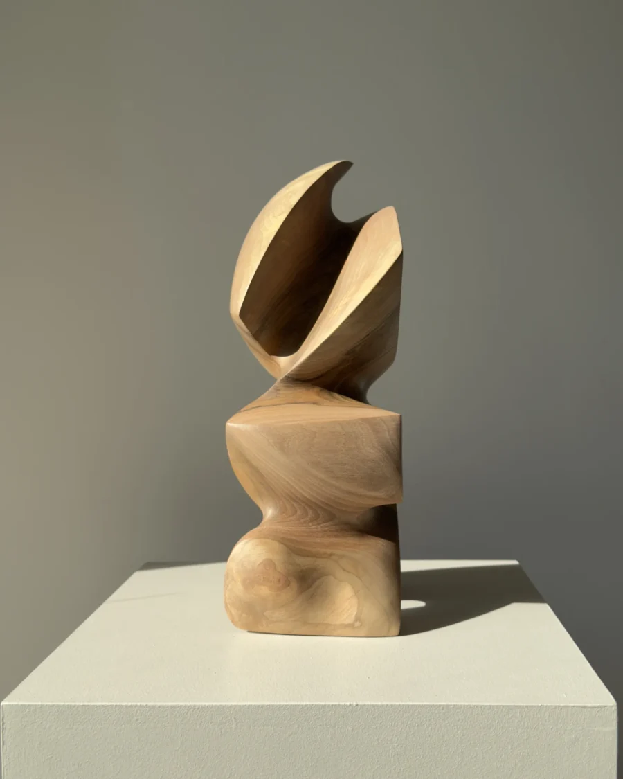 Abstract walnut wood sculpture Aureon standing on a white pedestal, showing its balanced vertical form and natural grain.