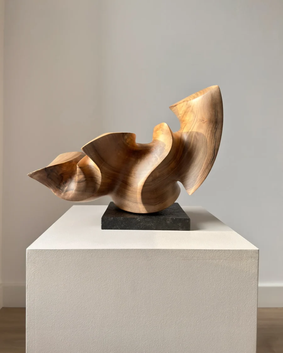 Confluence hand-carved walnut wood sculpture on a black granite base photographed in natural light.