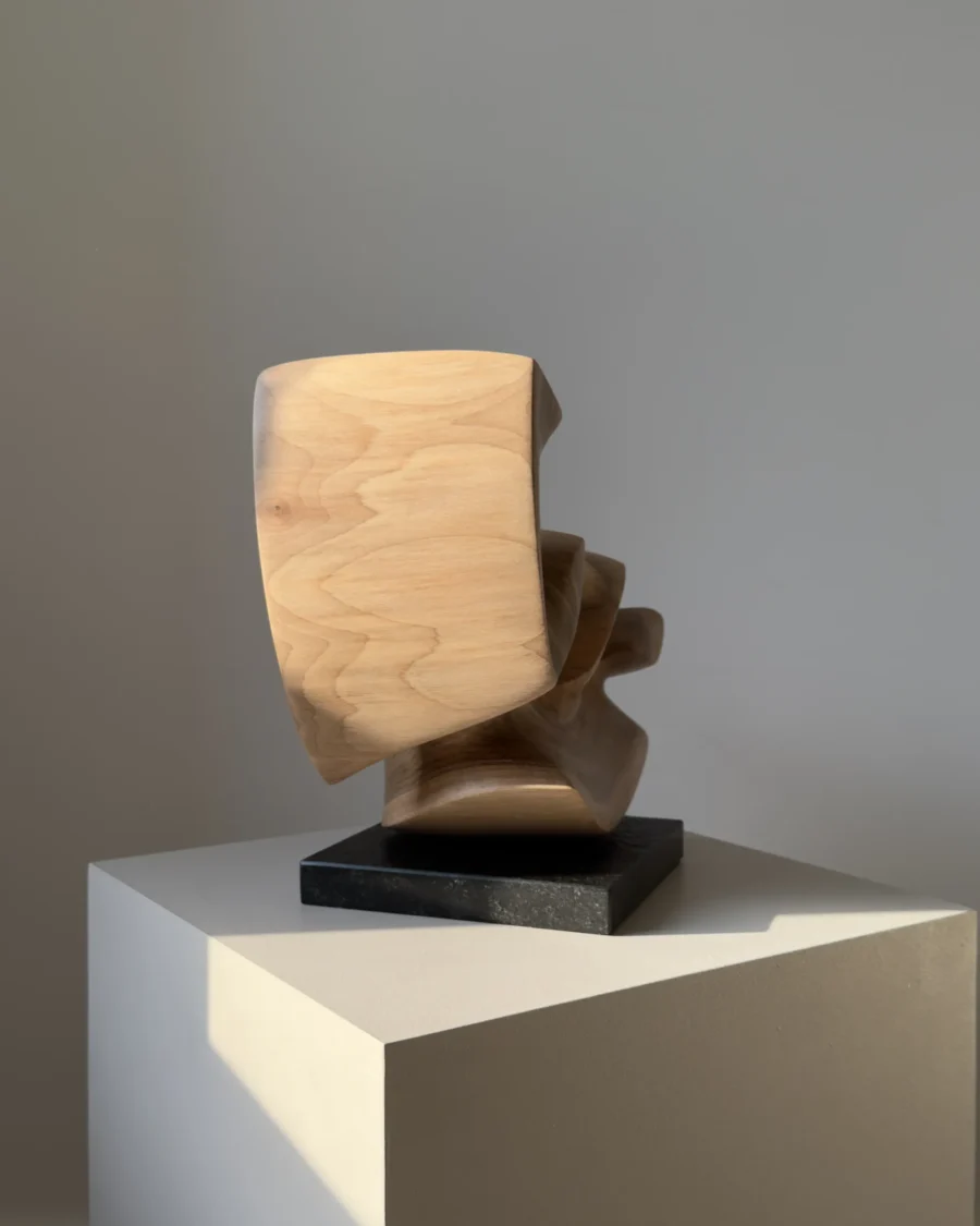 confluence-walnut-sculpture-side-profile-view-black-granite-base End view of Confluence abstract walnut wood sculpture showing layered curves and natural grain.