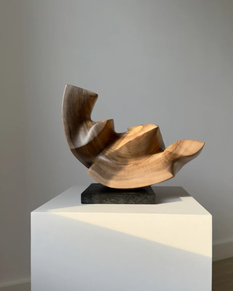 confluence-wood-sculpture-side-profile-walnut-art Profile view of Confluence abstract walnut sculpture on a black granite base in natural light.