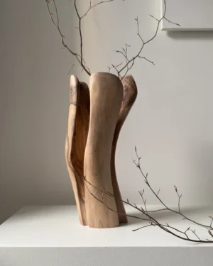 Dualis hand-carved walnut wood vase displayed with natural branches in a modern gallery-style interior.