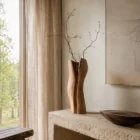 dualis-walnut-vase-modern-organic-interior Dualis hand-carved walnut vase displayed in a modern organic interior with natural light, linen curtains and minimalist décor.