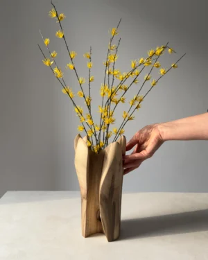 Hand carved walnut vase styled with decorative yellow flowering branches in natural light