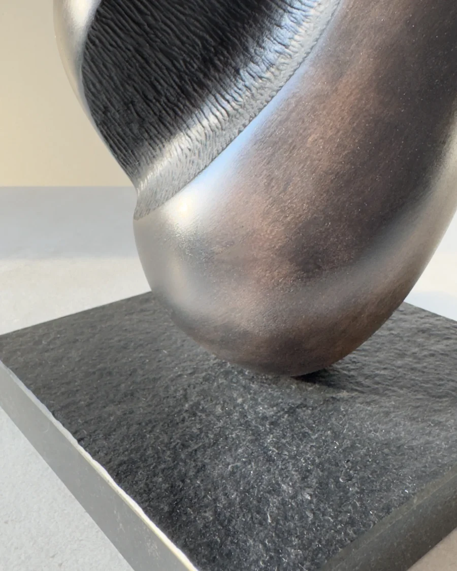 Detail of the black granite base and stainless steel rod supporting the hand-carved sculpture "Poise".