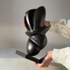 Full view of the original apple wood sculpture "Poise" displayed on a black granite base in natural light.