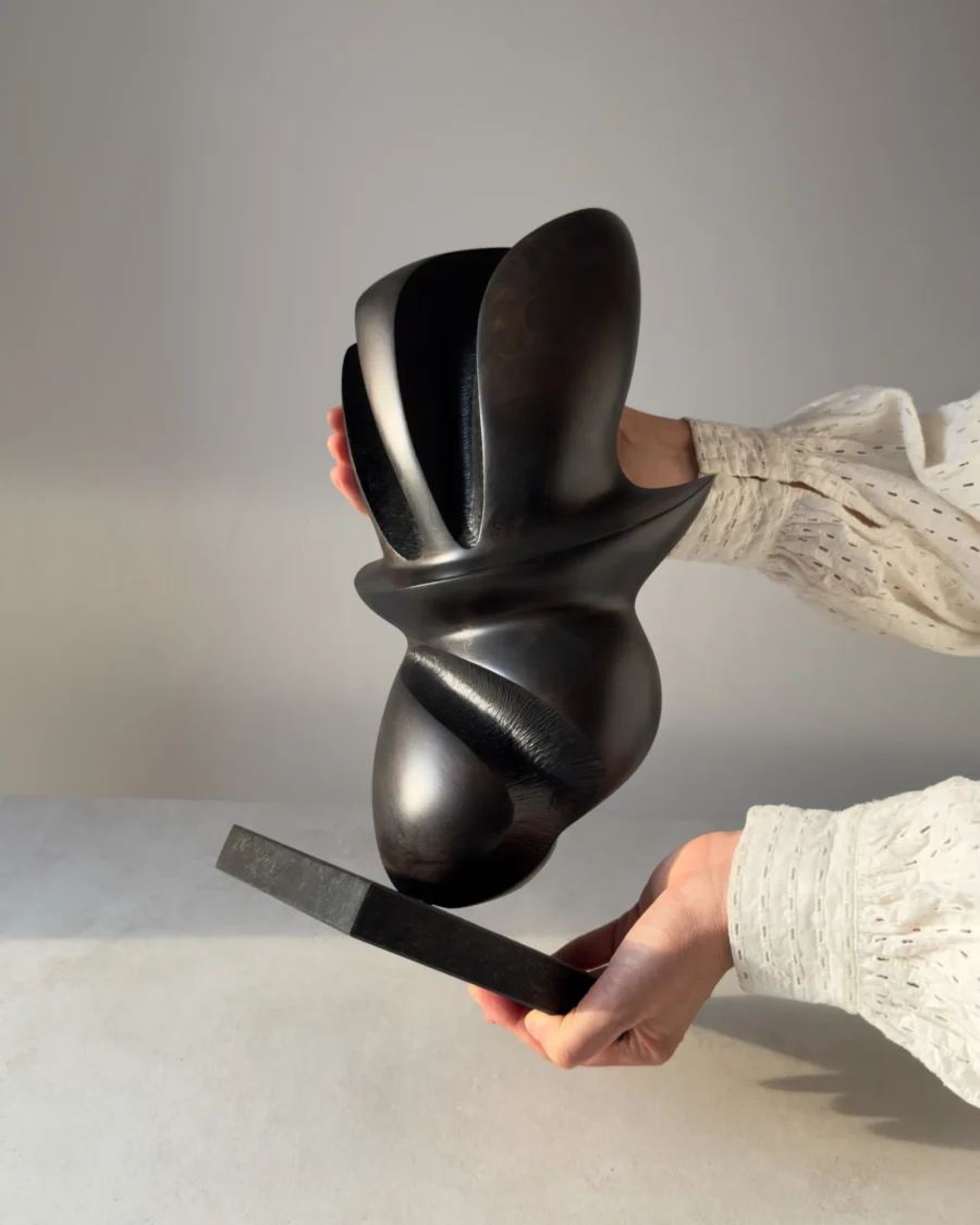 Full view of the original apple wood sculpture "Poise" displayed on a black granite base in natural light.