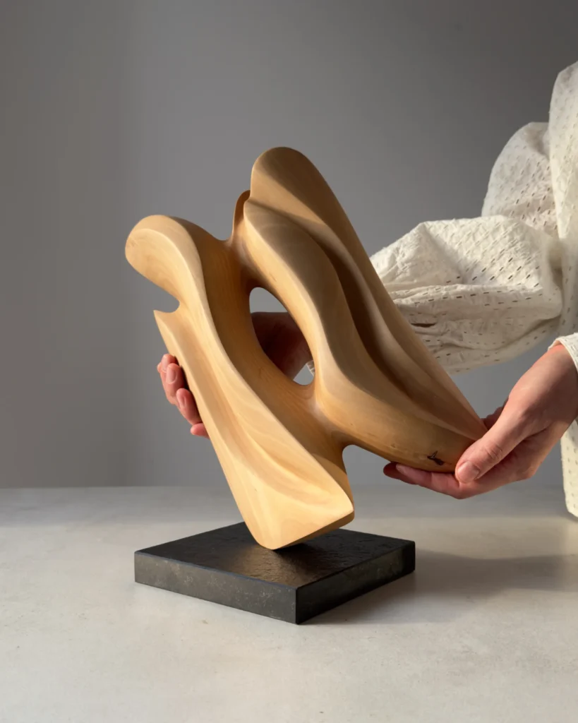Hand-carved apple wood sculpture "Sway" shown in scale, mounted on a black granite base.