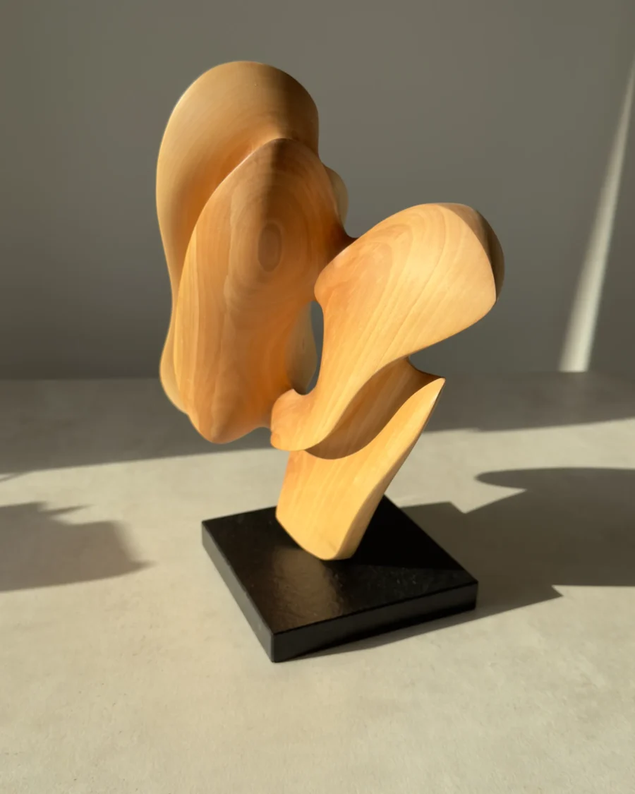 Hand-carved apple wood sculpture "Sway" photographed in natural daylight, revealing changing light across the smooth surface.