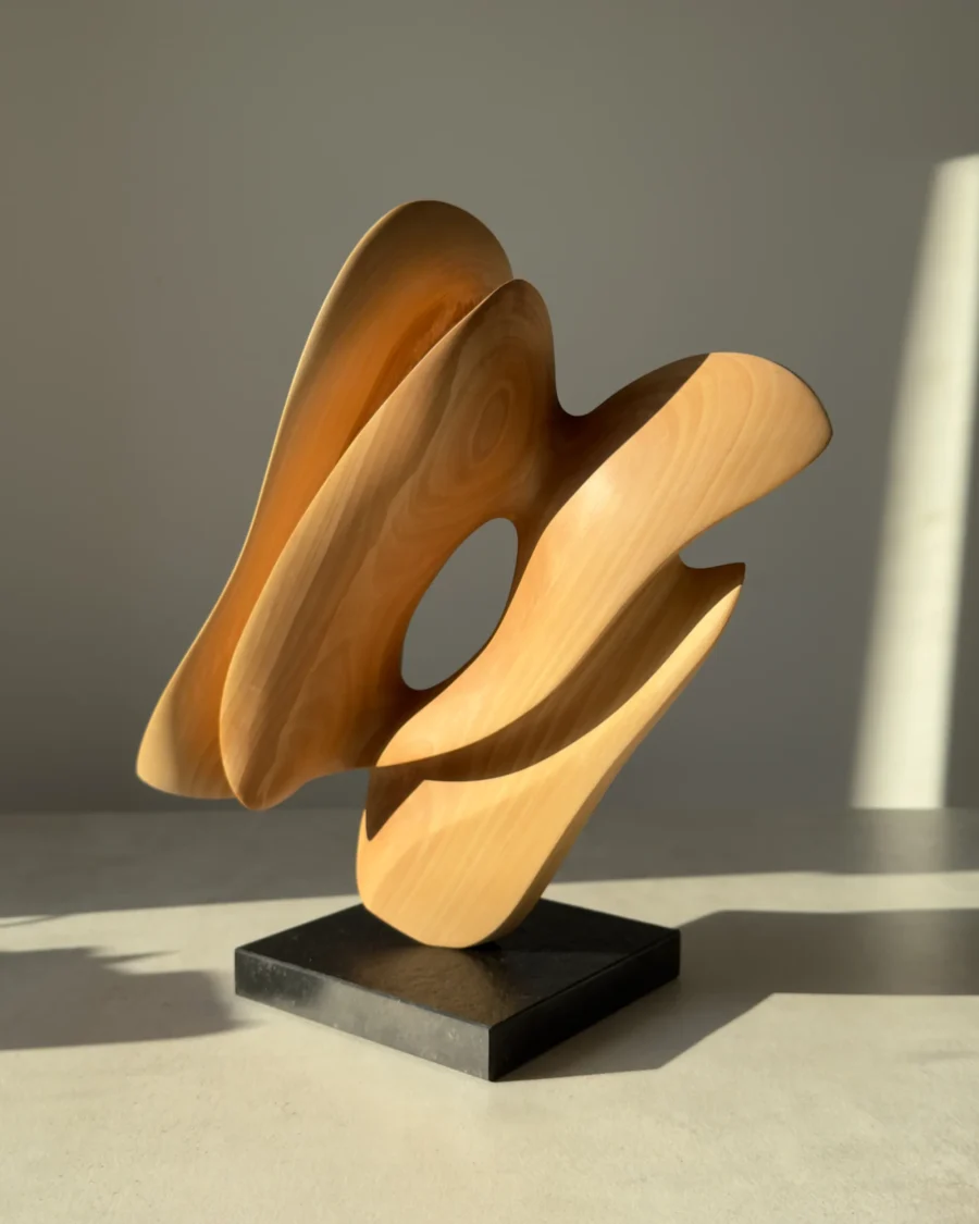 Side view of the one-of-a-kind hand-carved apple wood sculpture "Sway" on a black granite base in natural light.