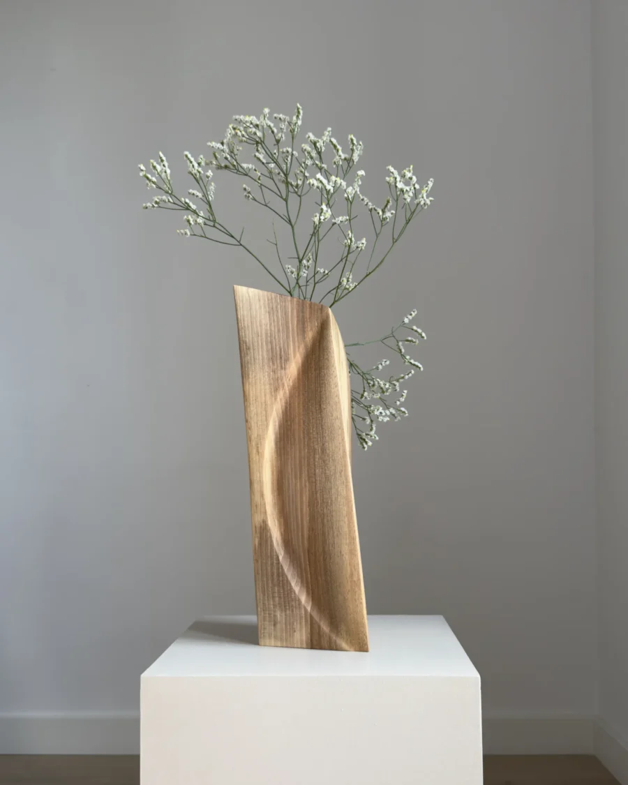 continuum-abstract-walnut-vase-curved-line-flowers Side view of Continuum hand-carved walnut vase with fresh white flowers, showing its tall slender profile and rounded edge.