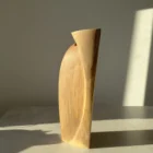 Narrow side view of the tall Continuum walnut sculpture, showing its slight lean and restrained natural colour.