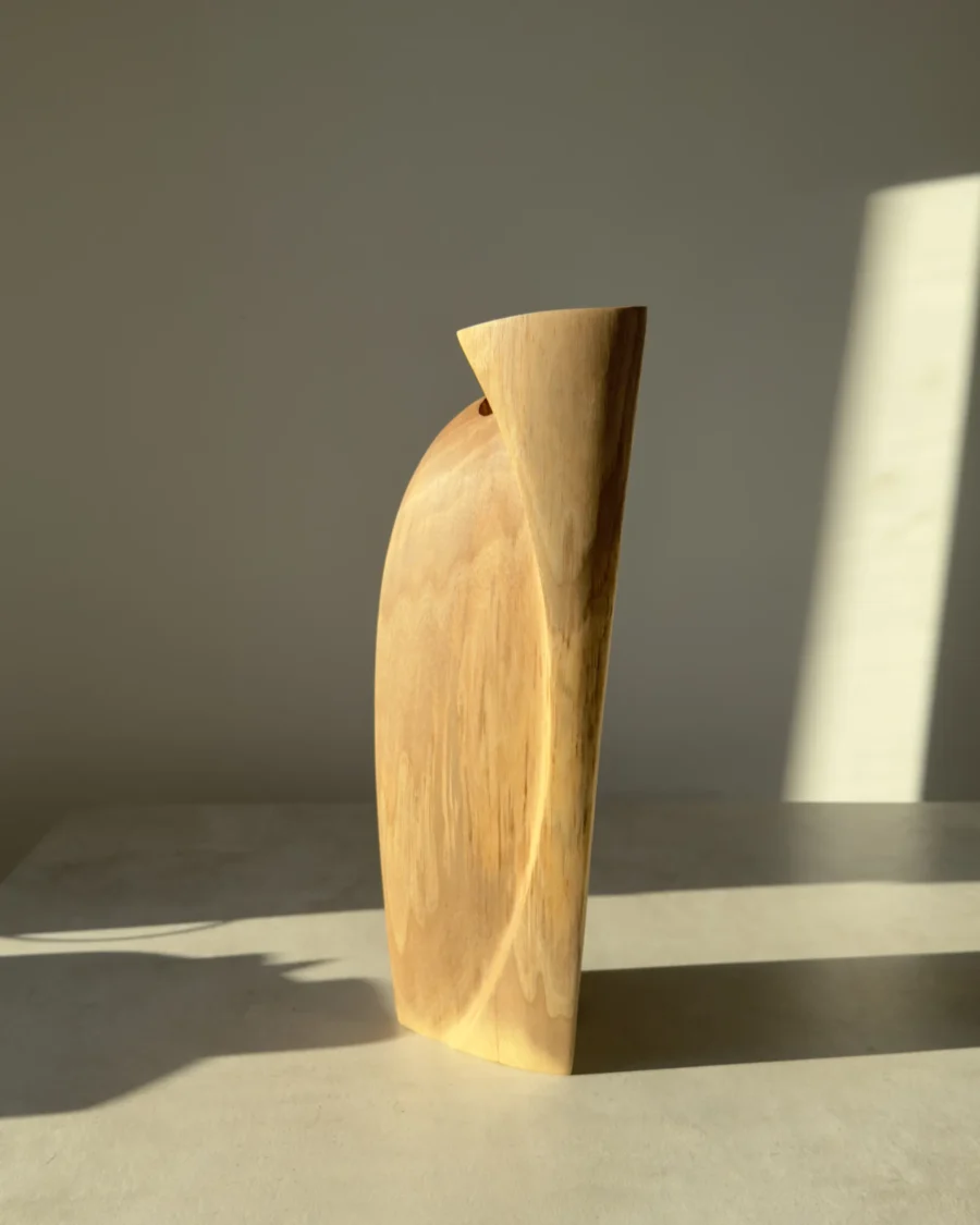 Narrow side view of the tall Continuum walnut sculpture, showing its slight lean and restrained natural colour.
