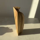 Side view of the Continuum walnut sculpture showing its curved volume, inclined top and discreet opening.