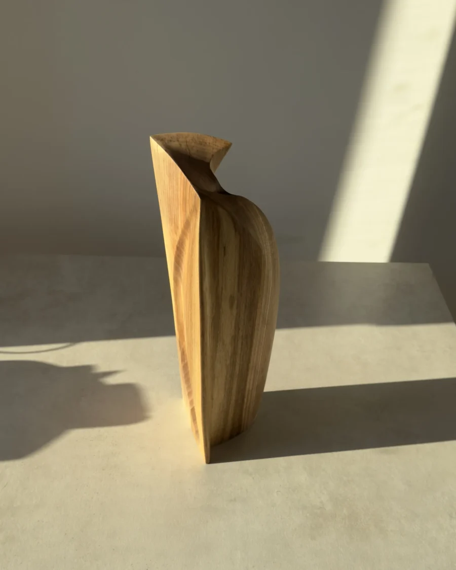 Side view of the Continuum walnut sculpture showing its curved volume, inclined top and discreet opening.