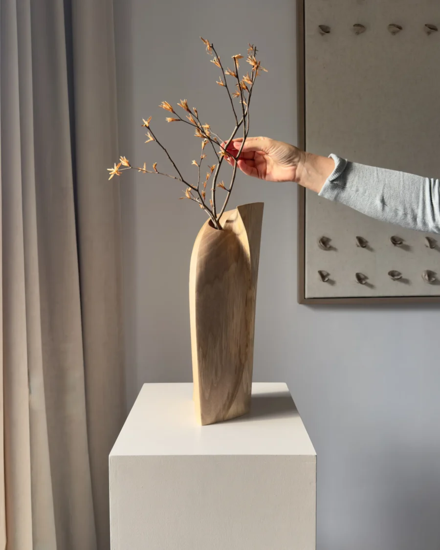 Hand arranging delicate branches in the Continuum walnut sculpture, demonstrating its use as a vase.
